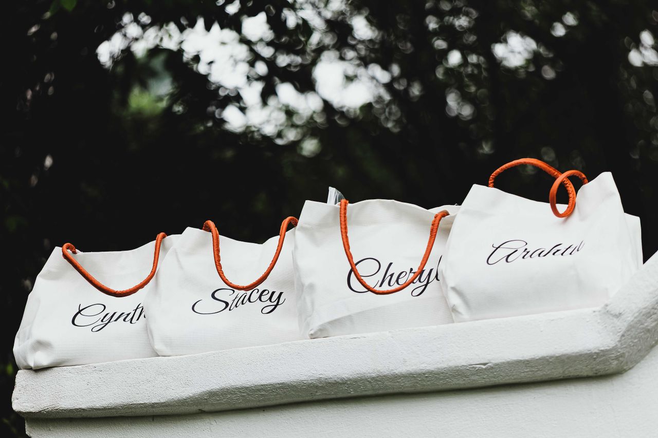 Four personalized tote bags with names and orange handles on display outdoors.